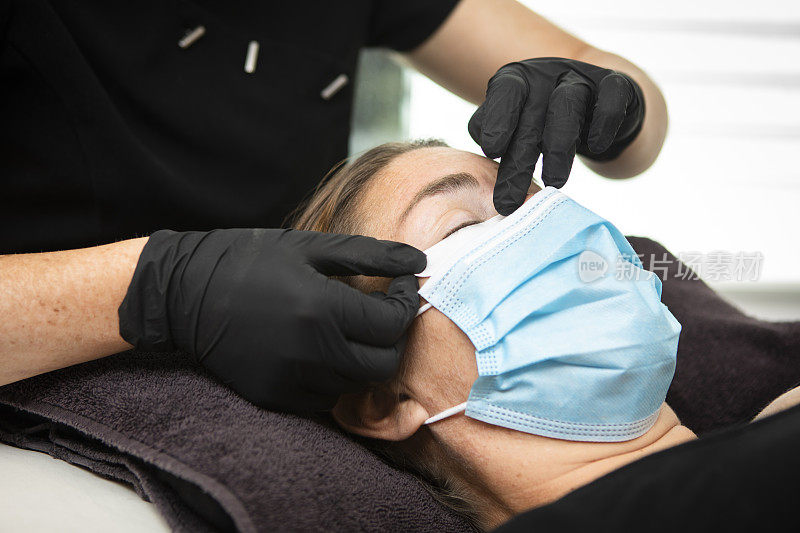 睫毛技师和客户在治疗过程中佩戴防护口罩和手套。