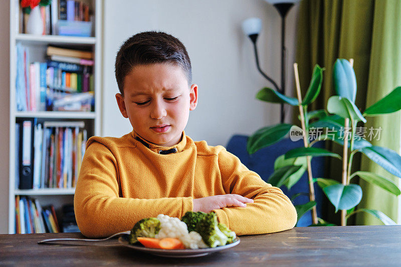 孩子对不得不吃蔬菜很不高兴。他的盘子里有许多蔬菜。他讨厌蔬菜。