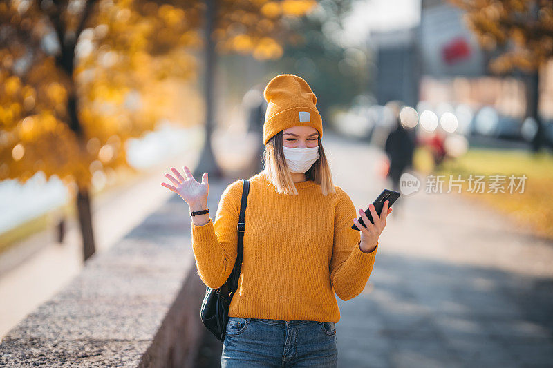 年轻女子戴着口罩在户外使用智能手机