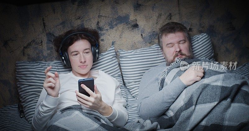 成熟的妻子在床上听音乐，而丈夫正在睡觉