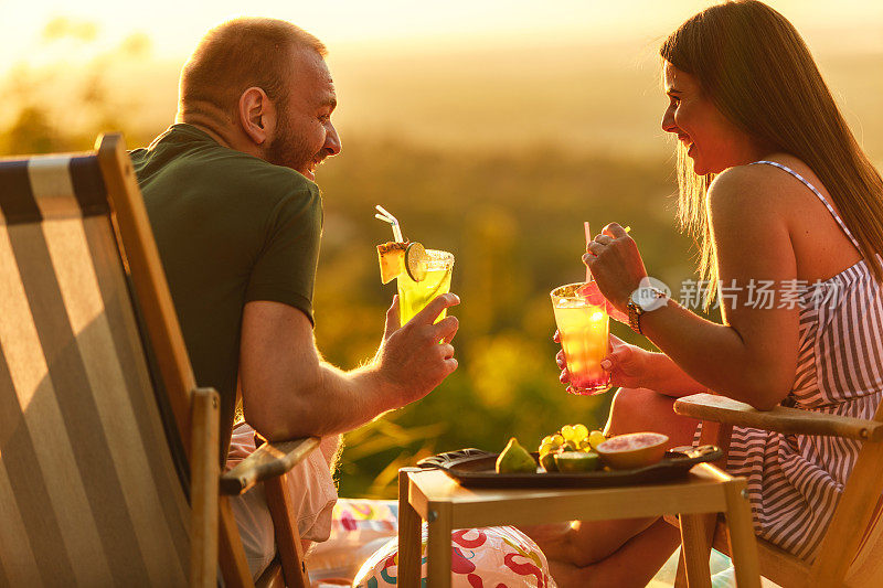 年轻的夫妇在甲板上享受夏日，鸡尾酒和充气