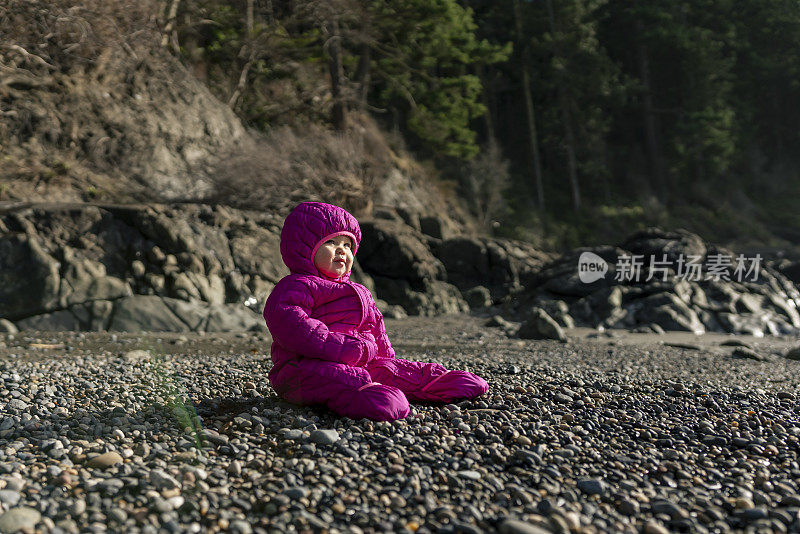 美丽的一岁小女孩独自坐在户外的海滩岩石上