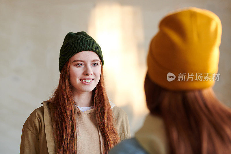 两名年轻女子的横向摄影照片，长红头发，戴着帽子站在对方面前微笑