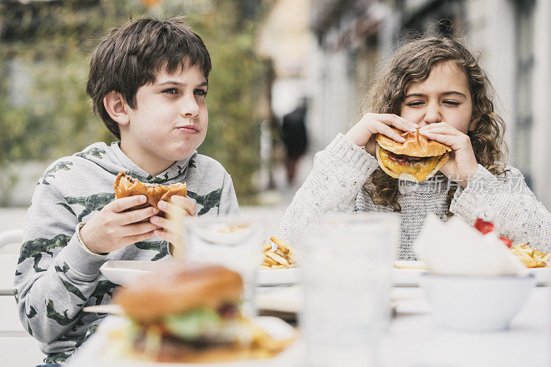 九岁的小女孩和小男孩在户外吃汉堡包。