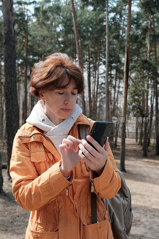 成熟的女人在森林里使用智能手机。半身肖像