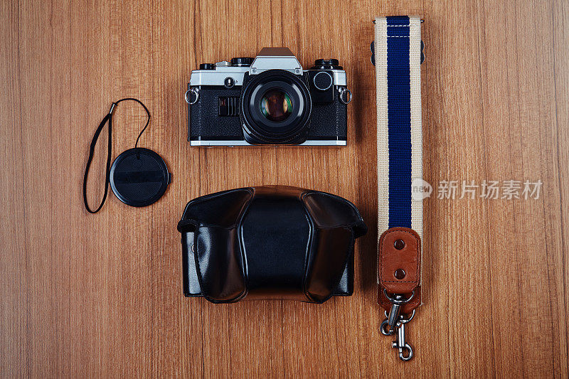 专业的老式单反模拟胶片相机，带背带，镜头盖和坚实的皮套在木桌上
