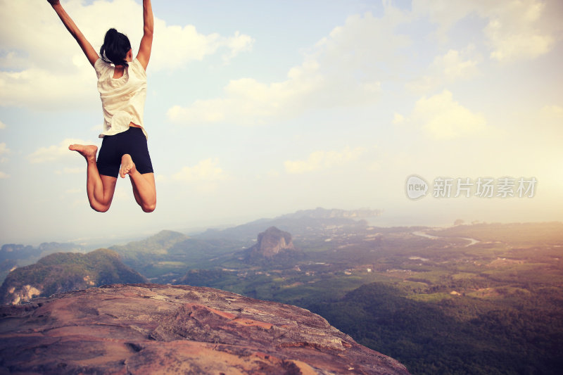 欢呼年轻的亚洲女子跳上山峰岩石