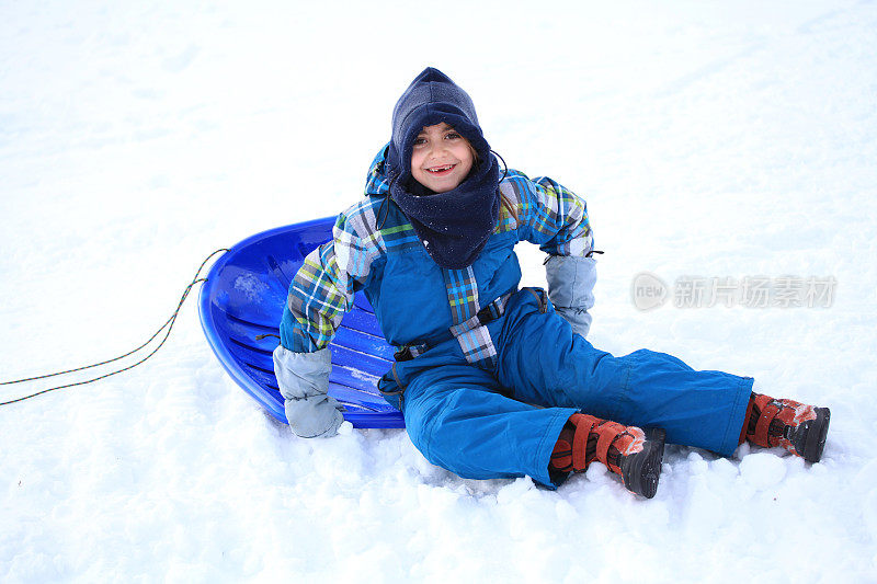 快乐的女孩穿着雪衣和塑料雪橇