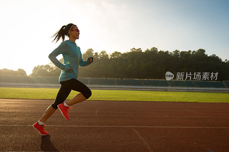 年轻女子在阳光明媚的早晨在体育场跑道上跑步