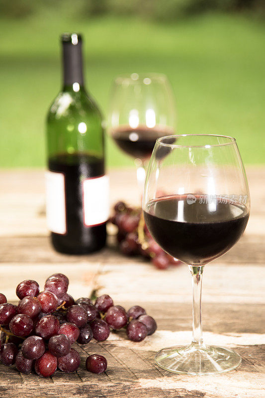 夏日红酒放在质朴的户外餐桌上。瓶,葡萄。