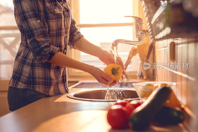 一个陌生的女人在厨房水槽里洗红辣椒。
