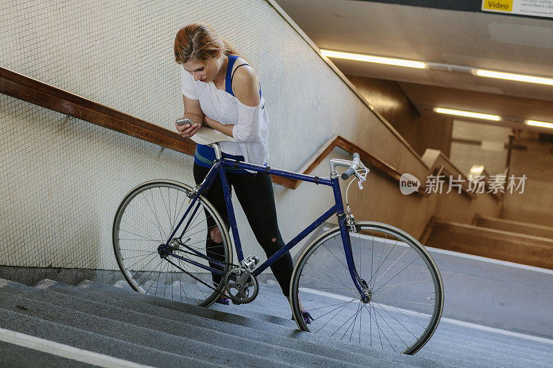 一个女人在地铁站用智能手机和自行车