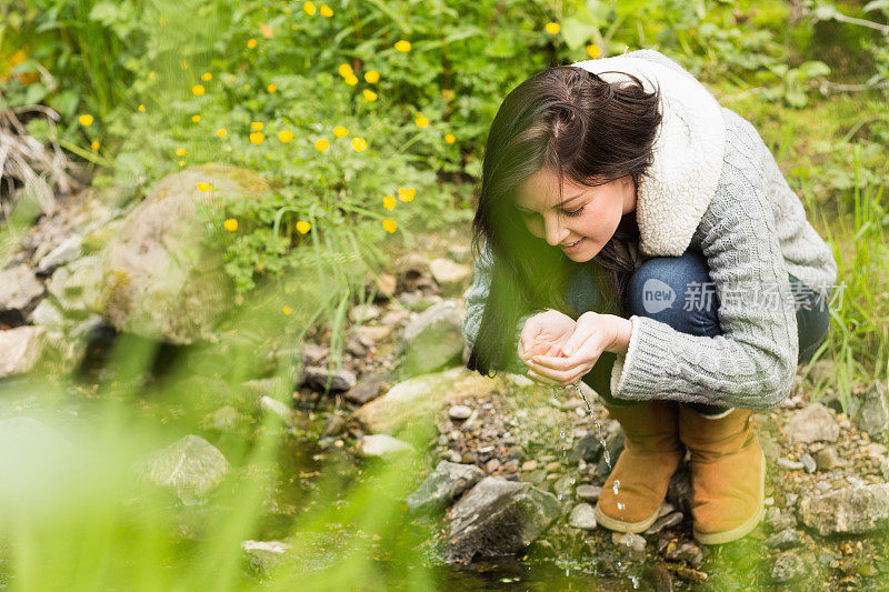 可爱的女人在森林小溪里喝水