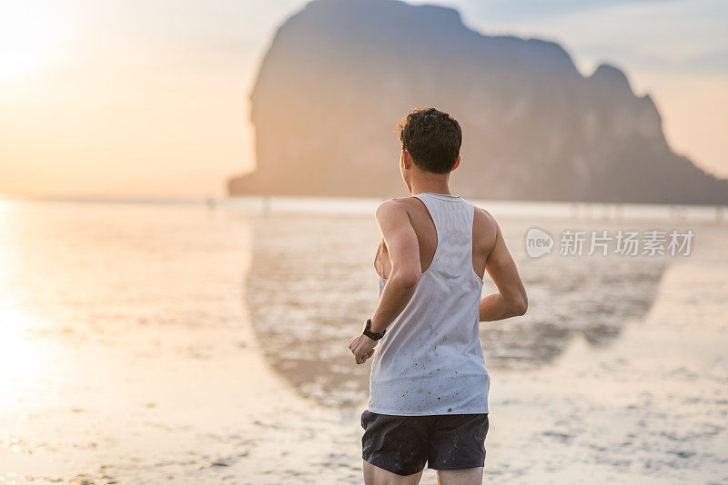 年轻的亚洲男子在海滩上奔跑，夕阳为背景