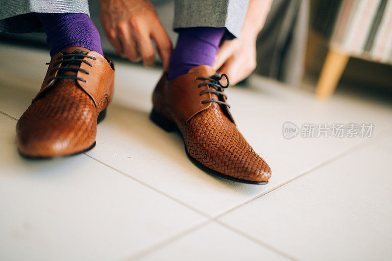 那个男人穿着灰色的休闲裤和紫色的礼服袜子和棕色的鞋子