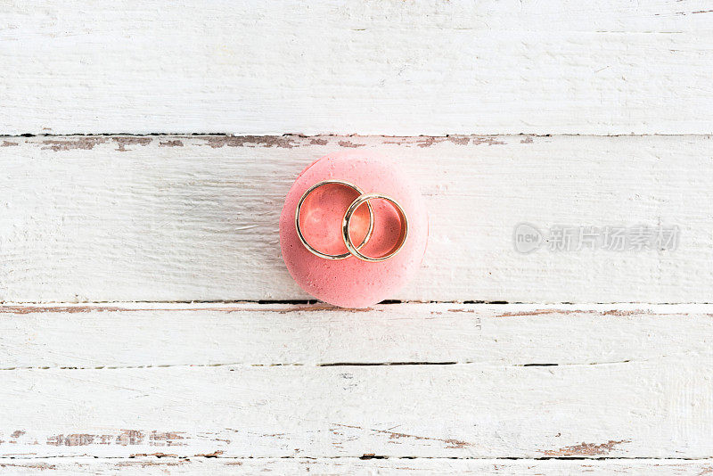 在木制桌面的粉红色马卡龙上闪闪发光的金色结婚戒指的俯视图