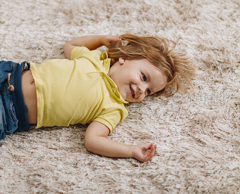 快乐的小男孩在家里柔软的地毯上休息。