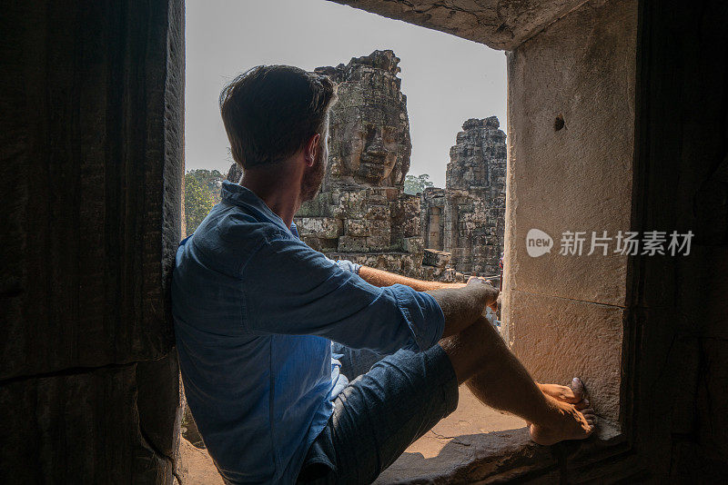 在柬埔寨吴哥窟建筑群中，一名年轻人从窗口眺望巴戎庙古庙
