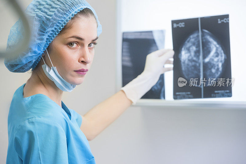 身着手术服的女医生或护士正拿着一张乳房x光片站在x光照明灯前
