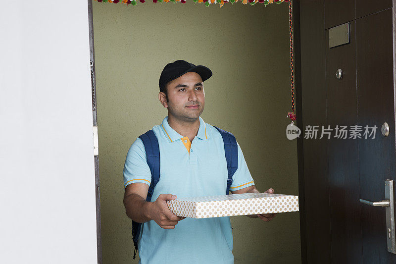一名年轻的快递员骄傲地站在住宅楼的走廊上，手里拿着一个快递包裹。