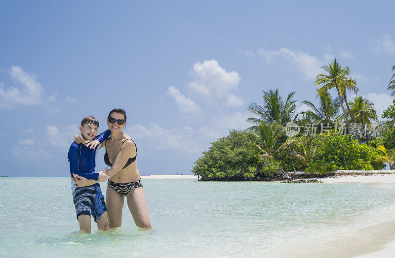 母亲和儿子有乐趣在浅水在小岛屿海滩四月，马尔代夫