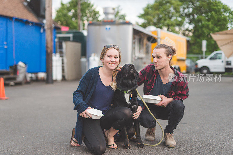 一对年轻夫妇抱着他们的狗和食品车上的打包盒摆姿势