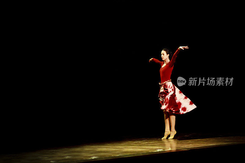 在黑色背景下，一名女子在空旷的舞台上跳芭蕾舞