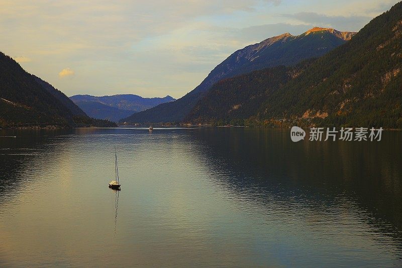 在奥地利戏剧性的黎明时分，一艘孤独的帆船与泰洛阿尔卑斯一起行驶在阿钦湖上