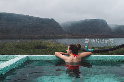 在冰岛的峡湾景色中，一个女人在热水池里洗澡