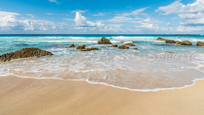 海浪冲刷着沙滩，嶙峋的石头露出水面