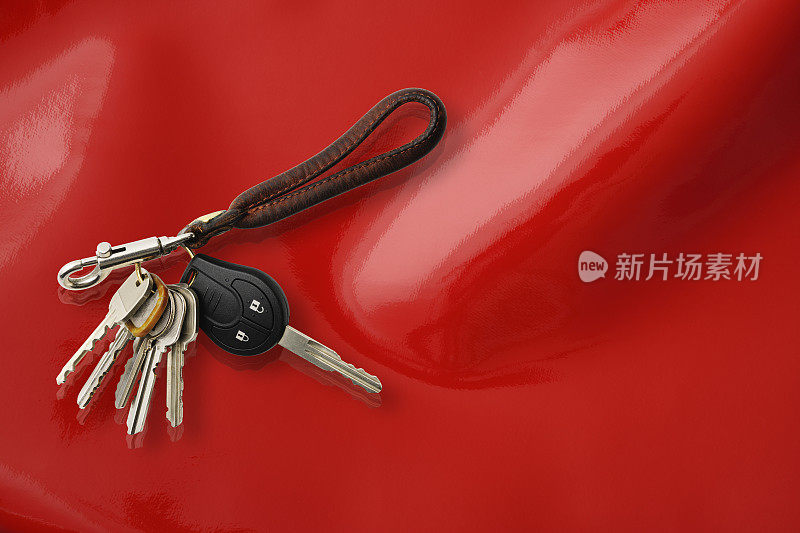一串钥匙与皮革钥匙圈在闪亮的红色乙烯基背景