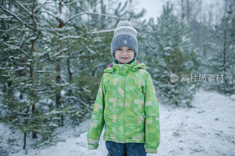 冻僵的男孩穿着暖和的衣服，带着期待已久的第一场雪，在森林里漫步，冬天的仙境