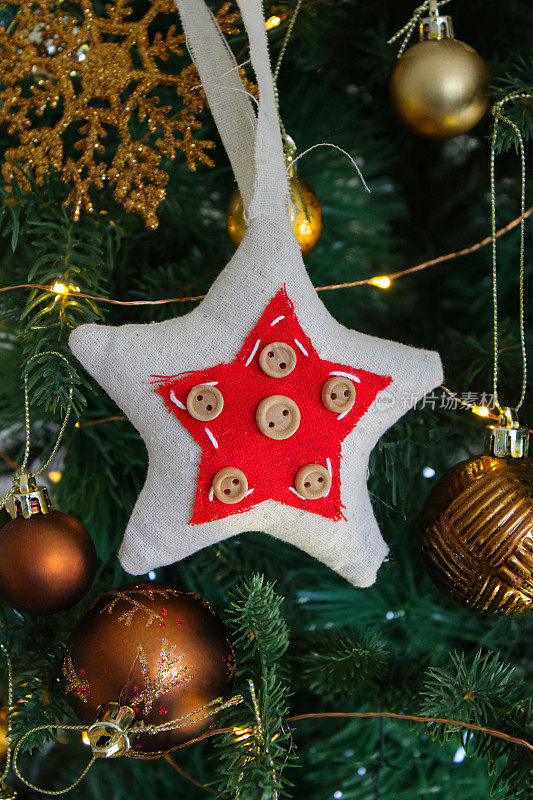 图像的毡和钮扣星装饰周围的金和铜彩色的小装饰物挂在人造圣诞树树枝上，雪花，云杉针，模糊的白色仙女灯的背景