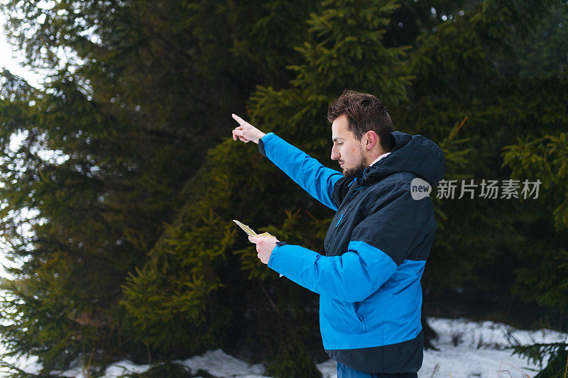 年轻的男性徒步旅行者穿着蓝色夹克，在雾蒙蒙的雪山中迷失了方向，看着地图