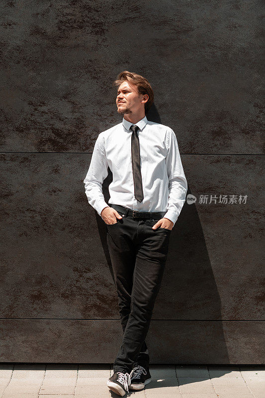 一名刚起步的商人，身穿白衬衫，系着黑领带，站在灰色的墙前