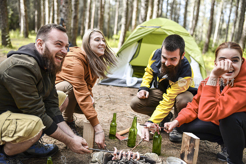 微笑的朋友享受野营和准备烧烤串
