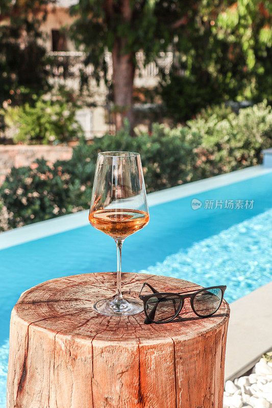 Rosé木桌子和游泳池上的酒杯
