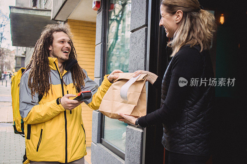 留着脏辫的年轻快递员在餐厅门前拿起一个包裹