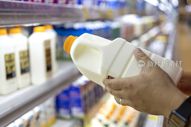 一名男子的手从超市乳制品区拿起一瓶有机鲜奶
