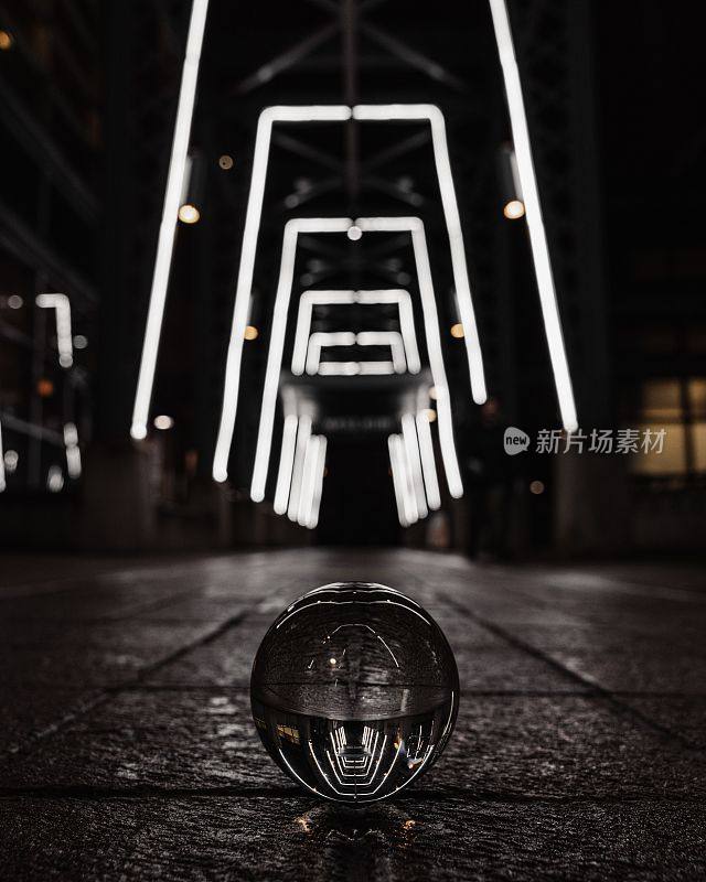 地面上的透明玻璃球在夜晚反射出隧道走廊的发光框架