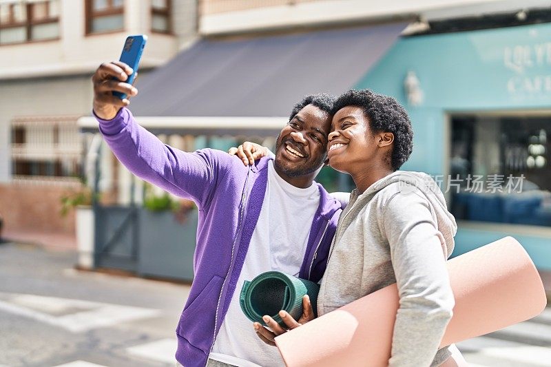 非裔美国人夫妇抱着瑜伽垫在街上用智能手机自拍