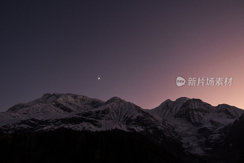 彩色浪漫的夜空在群山之上。白雪皑皑的山峰映衬着星空的背景。