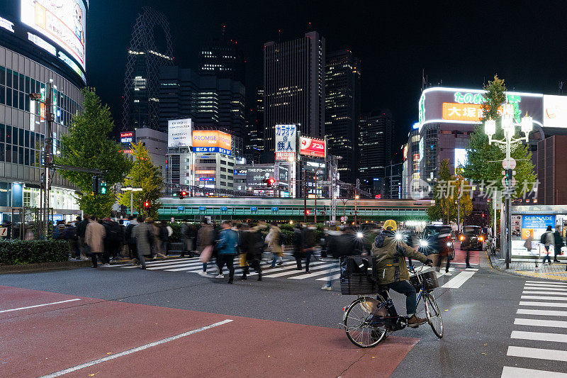 夜间运动模糊的火车交通运输，日本人走过斑马线在歌舞伎町日本东京新宿，办公大楼的城市景观。亚洲交通，亚洲城市生活理念