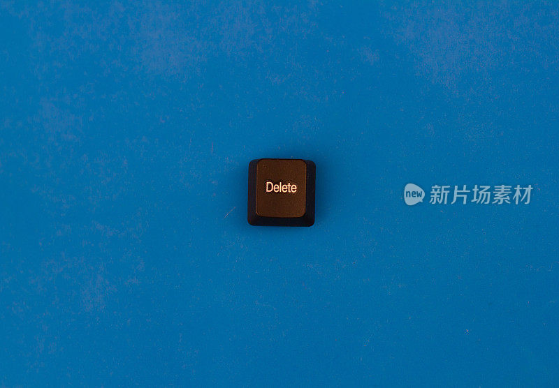 从隔离在蓝色背景上的计算机键盘上删除按钮。一个带有“删除”字样的黑色按钮位于蓝色背景上，与键盘分开。