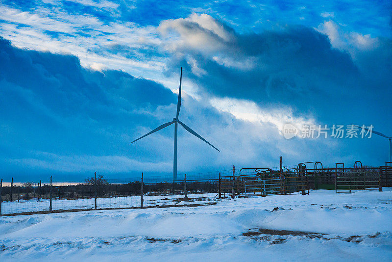 这张照片捕捉到了阴云密布的冬季风景中风车的美丽。白雪覆盖的地面与灰色的天空形成了鲜明的对比，而风车则巍然矗立在大自然的映衬下。