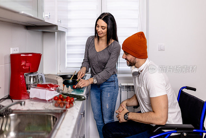 有爱心的年轻女子在准备饭菜时为轮椅上的男子提供支持和帮助