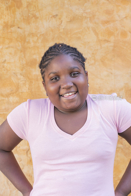快乐的年轻美国黑人女孩的肖像在户外墙的背景前微笑