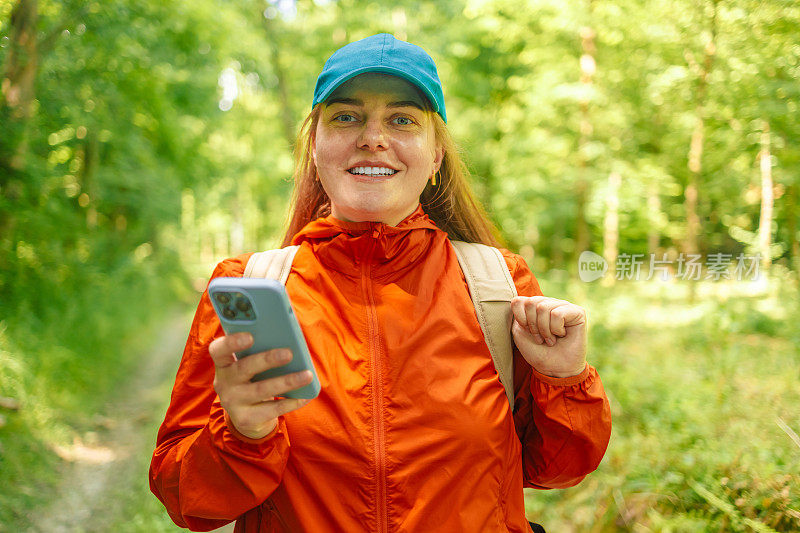 有吸引力的健康女孩游客与一个背包使用手机，而在森林里散步，做徒步旅行。远足时使用电子设备。
