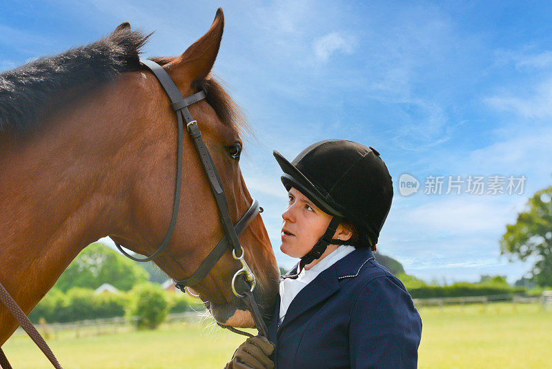 美丽的女骑手和她美丽的海湾马的特写镜头，在英国农村参加骑马比赛之前分享了一个激动人心的时刻