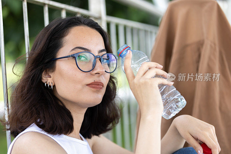 戴眼镜的年轻女子正在喝水。